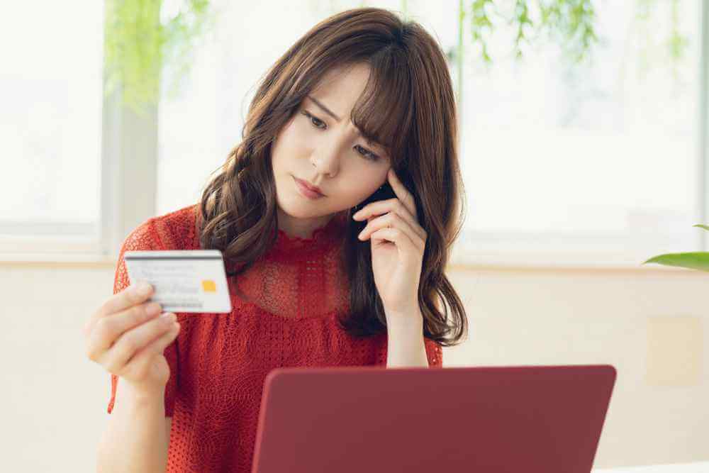 wanita dengan baju merah sedang berpikir bagaimana cara melunasi utang dari kredit yang macet