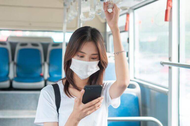 Asian,Girl,Wearing,Mask,While,Using,Smartphone,On,Bus